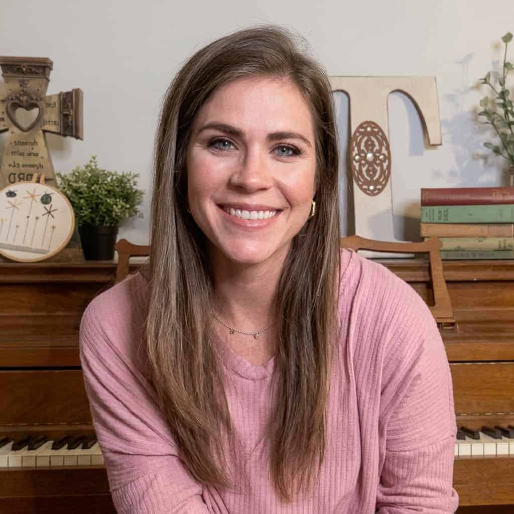 Jaimie Thomas - Simply Learning Together Jaimie Thomas smiling at a piano with decorative items and books in the background.